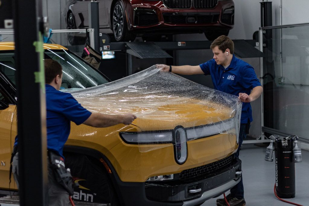 Two men are wrapping a yellow car with plastic wrap in a garage.