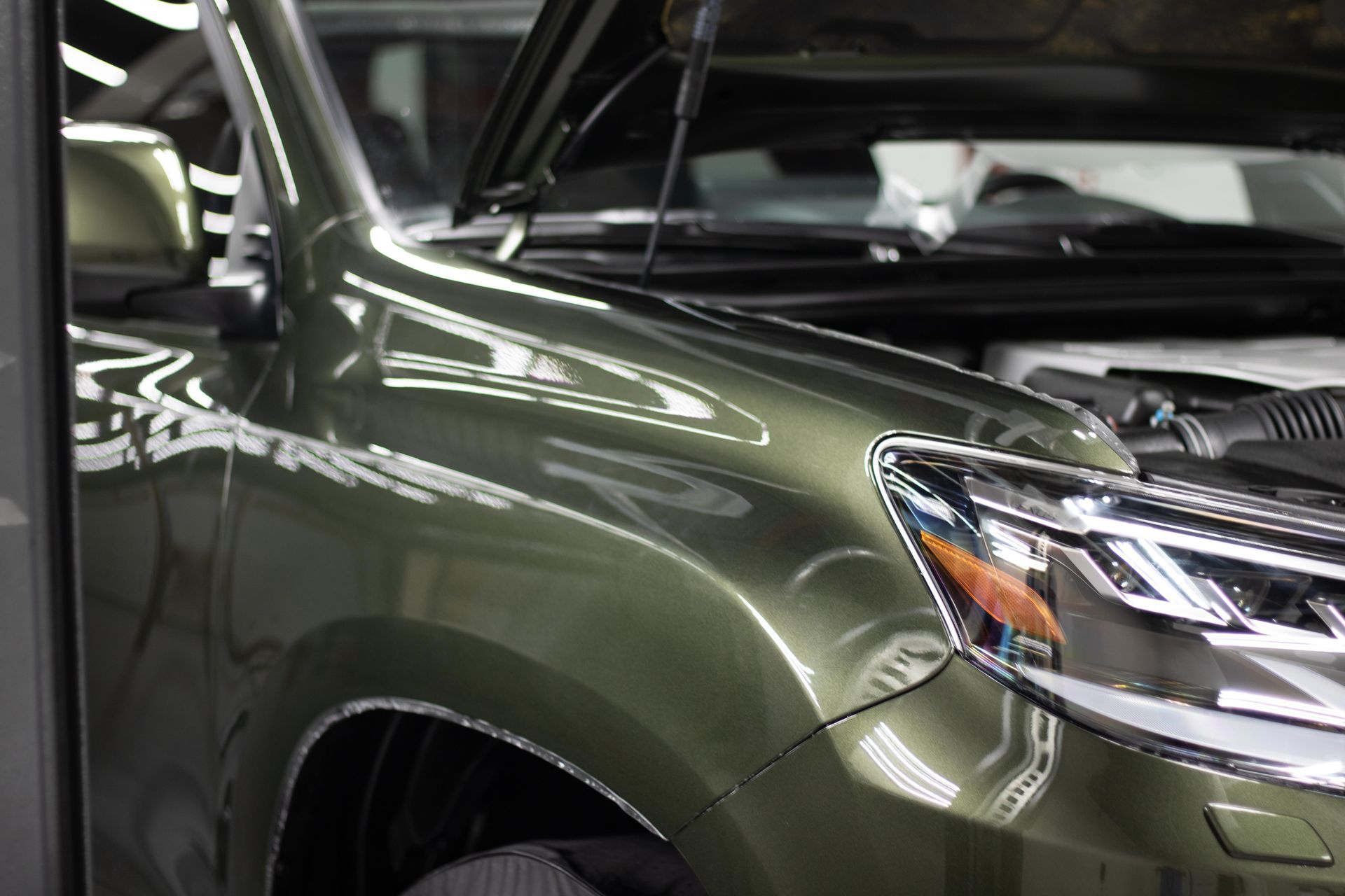 A green suv with the hood up is parked in a garage.