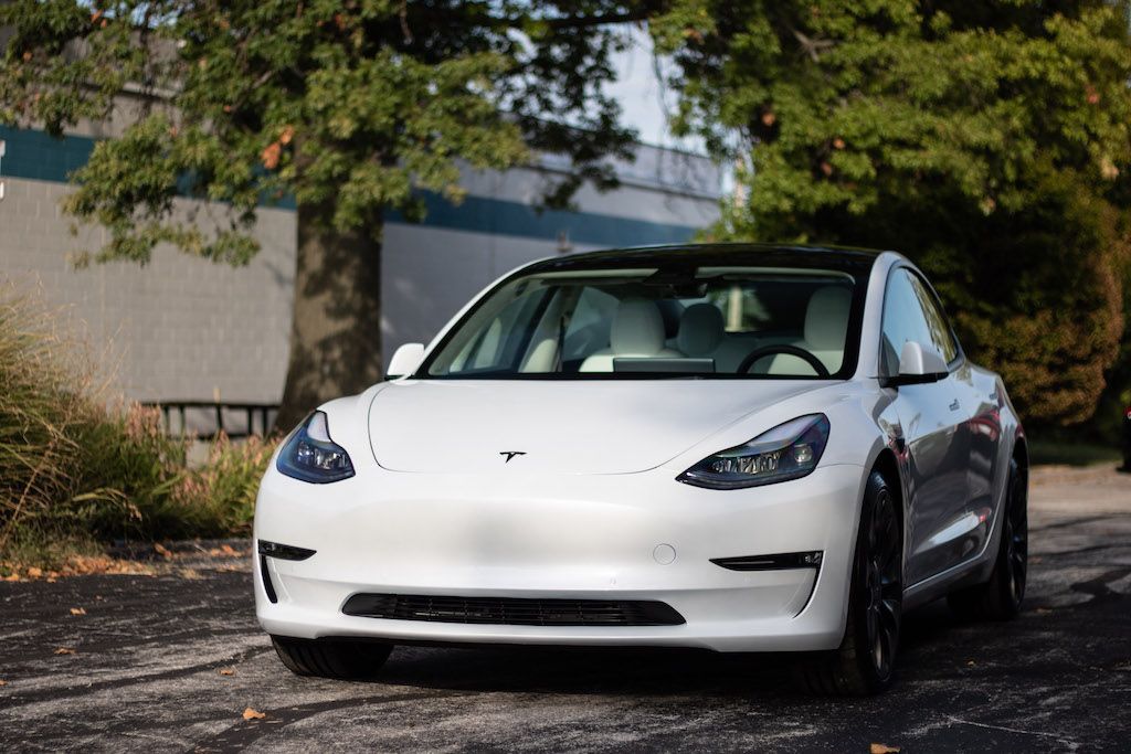 A white tesla model 3 is parked in a parking lot.