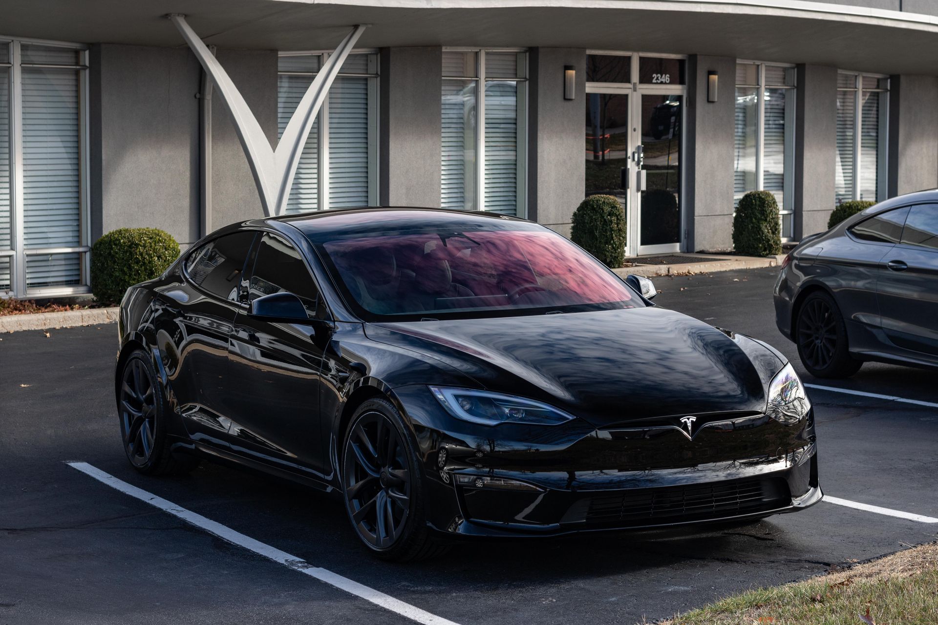 A black tesla model s is parked in a parking lot in front of a building.