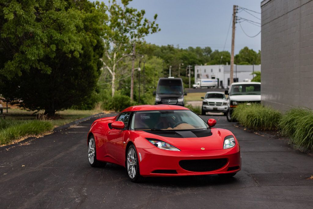 A red sports car is driving down a road next to a building.