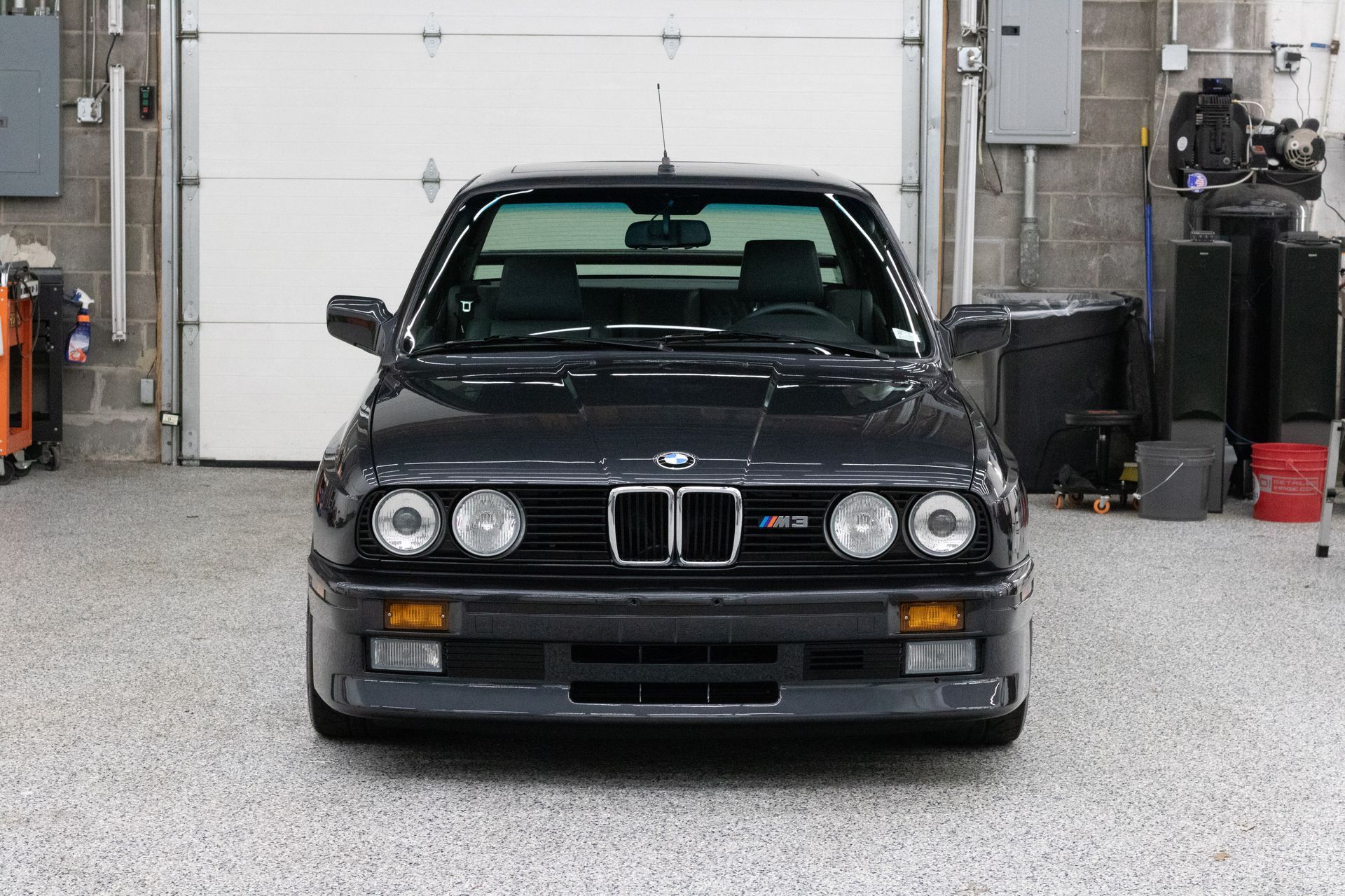 A black bmw is parked in a garage next to a garage door.