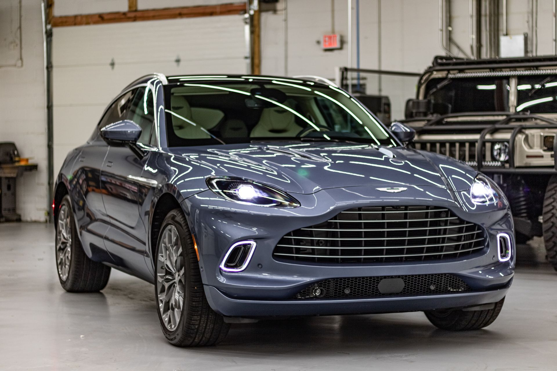 A gray aston martin dbx is parked in a garage next to a jeep.