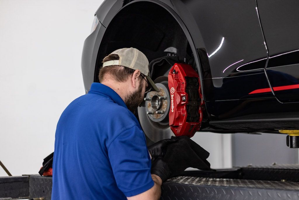 A man in a blue shirt is working on a car on a lift.