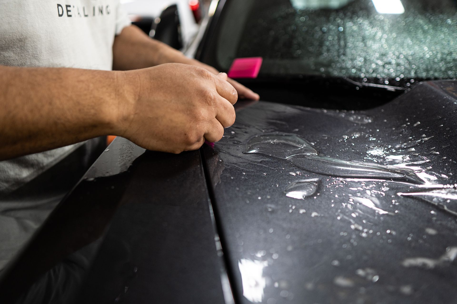A man is applying a protective film to the hood of a car.