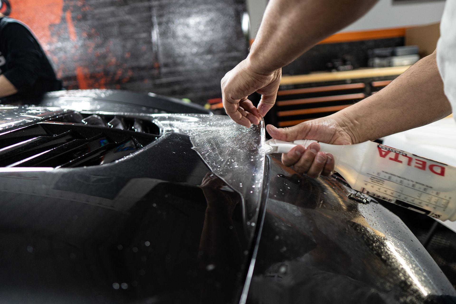 A person is applying a protective film to the hood of a car.