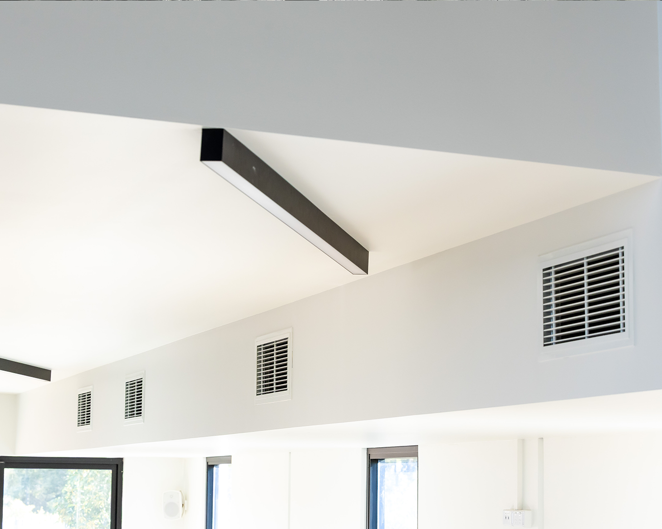 Modern white interior ceiling with exposed black light fixture and wall vents above windows