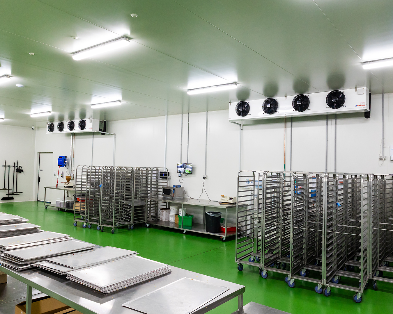 Bright commercial kitchen with stainless steel racks, tables, and trays on a green floor