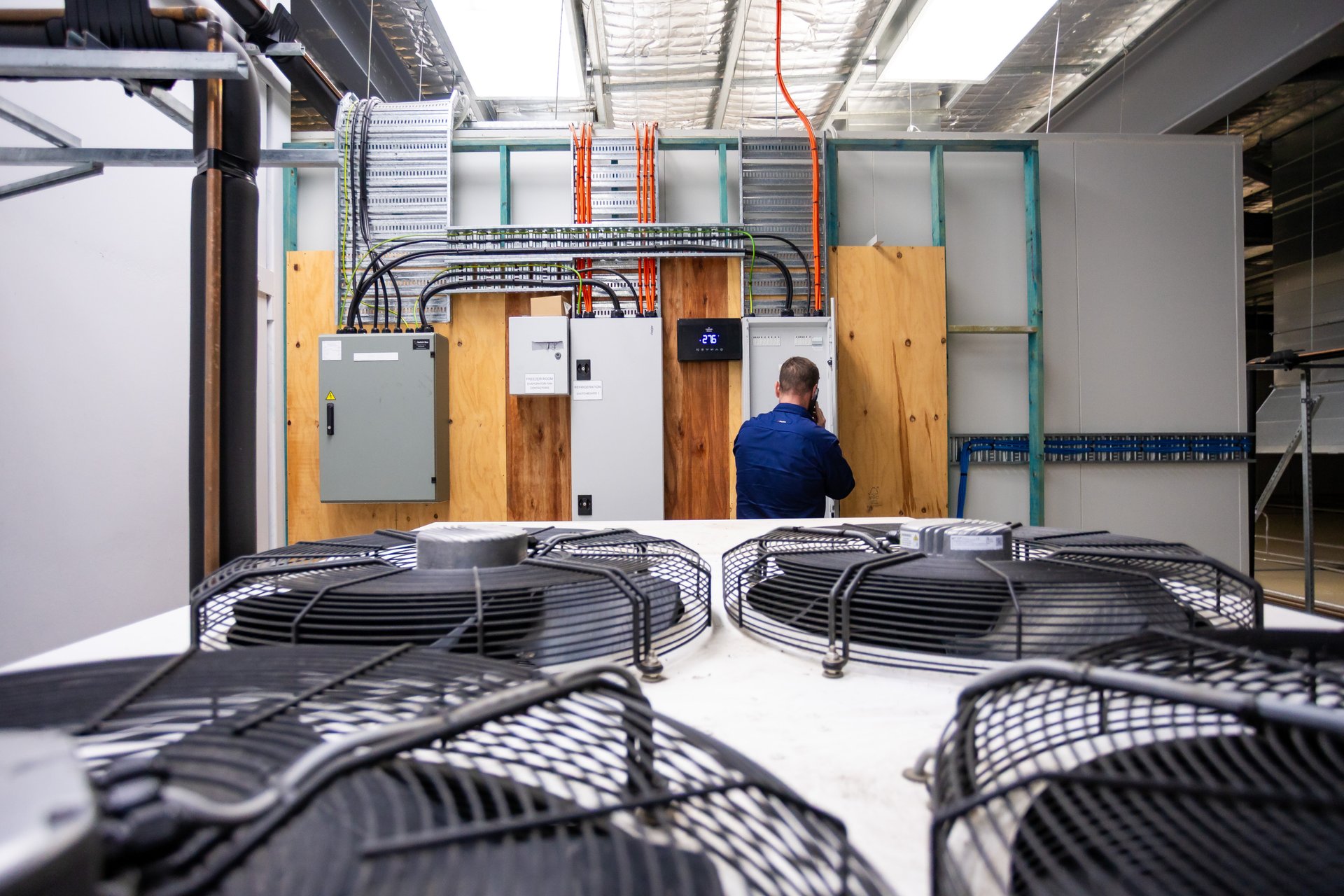 Industrial room with large cooling fans in foreground and a worker at electrical cabinets in the back