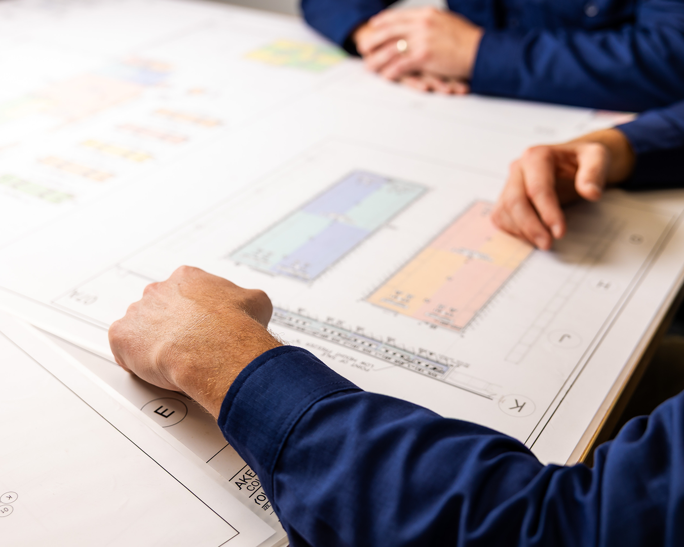 Two hands in blue sleeves pointing at a printed chart on a white desk