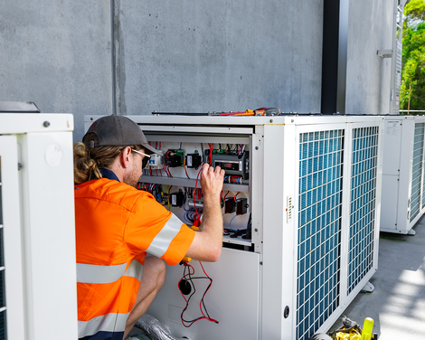 Technician in orange vest inspecting HVAC unit beside a building outdoors