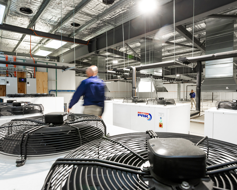 Industrial factory interior with a worker in blue near large machinery and coiled black cables