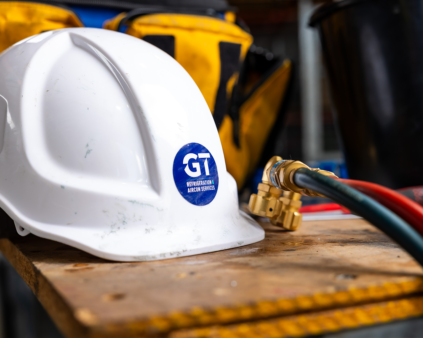 White hard hat on wooden surface with brass hose fitting and blue hose in a workshop setting