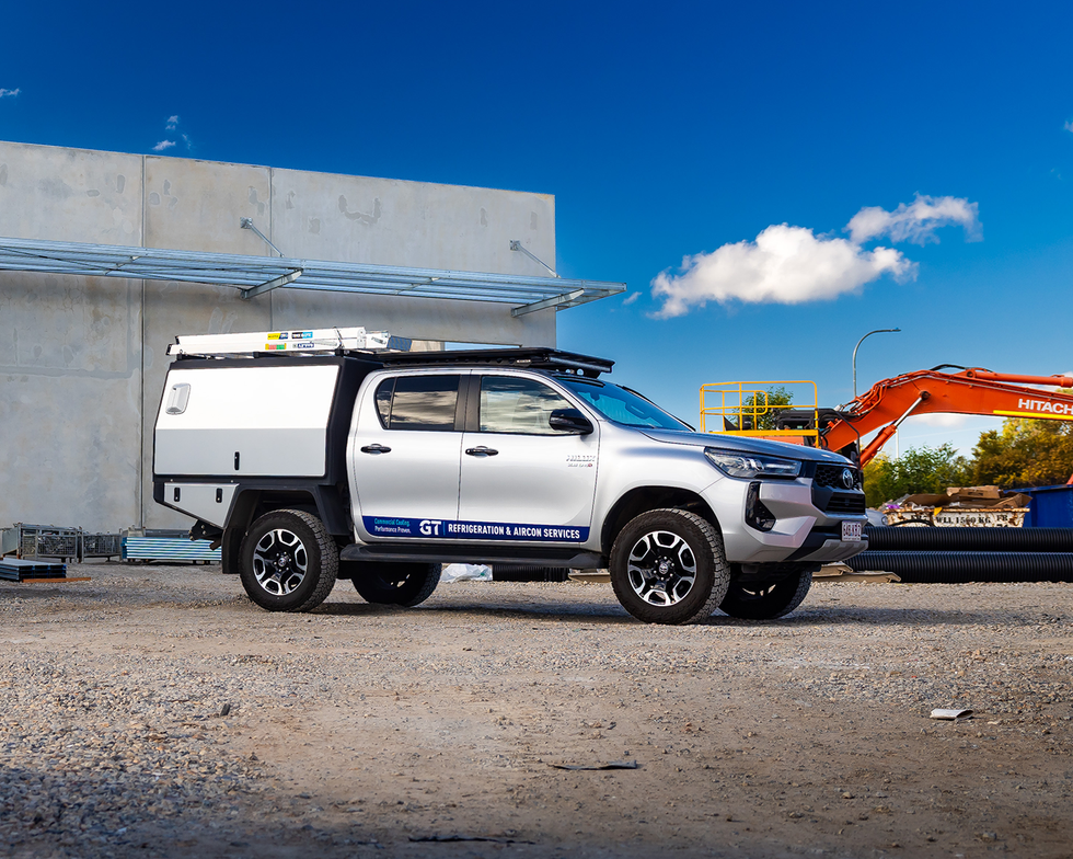 White pickup truck with canopy parked on gravel near a building under a blue sky