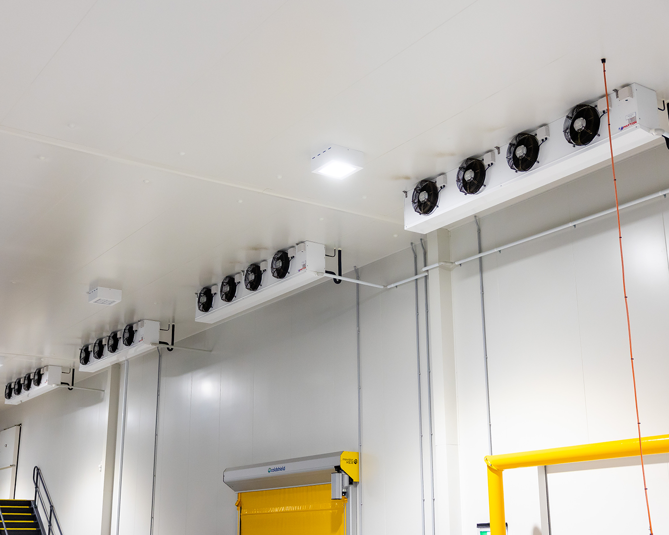 White industrial room ceiling with rows of black ventilation fans and yellow equipment below