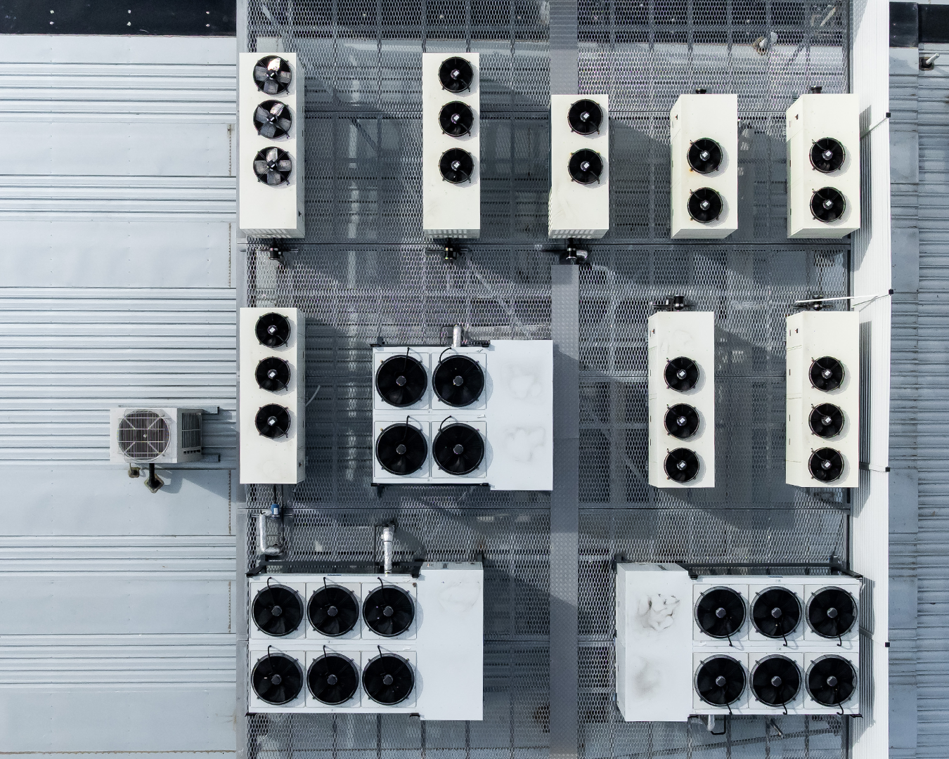 Rooftop air-conditioning units arranged in rows on a gray industrial building roof.