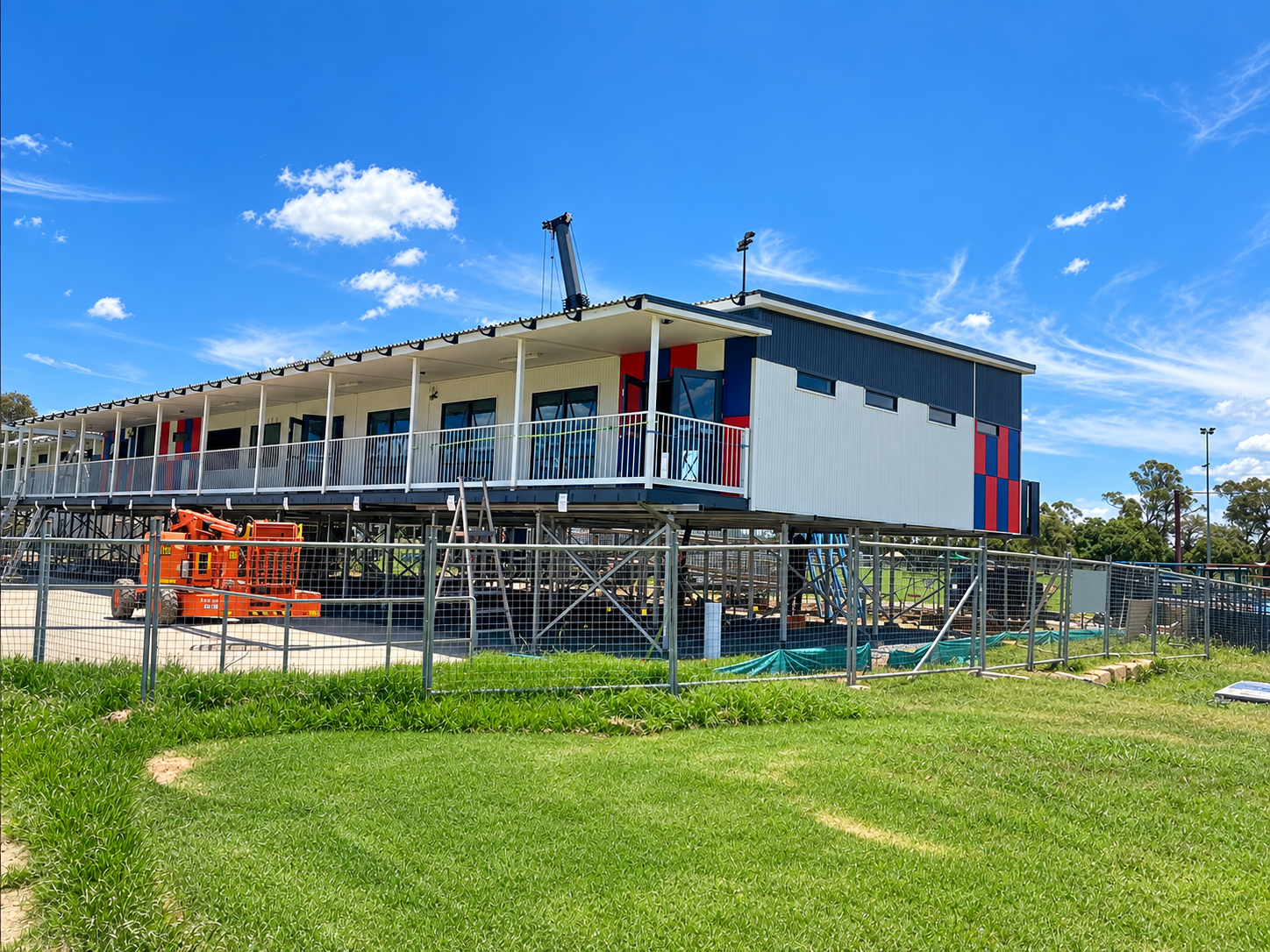Construction site with a partially built two-story building, scaffolding, and orange lifts under a blue sky