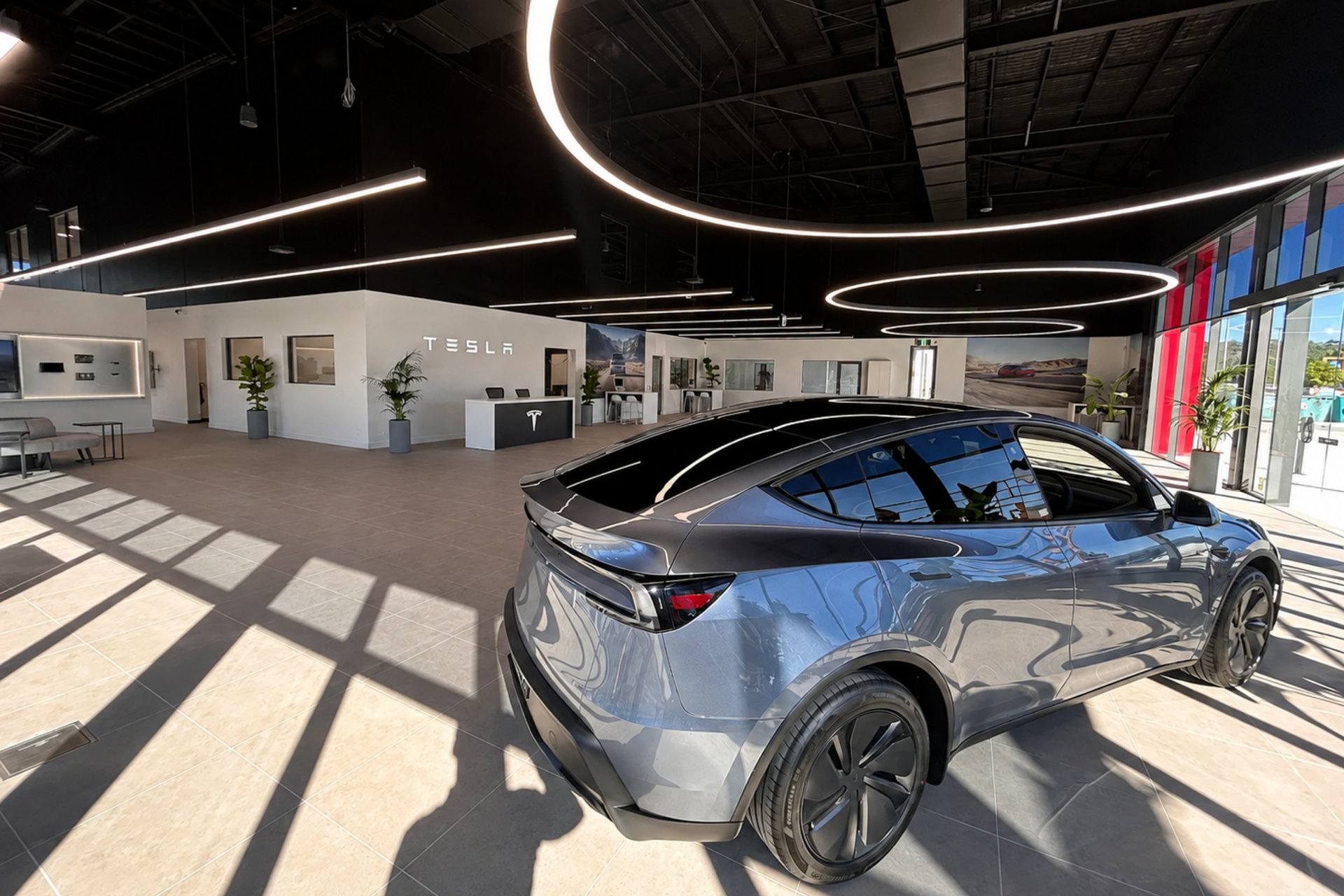 Silver Tesla SUV in a bright showroom with large windows and curved ceiling lights