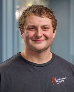 Smiling person in a dark gray T-shirt standing indoors against a blurred background