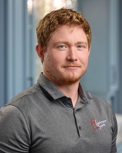 Portrait of a man in a gray polo shirt standing indoors against a blurred office background