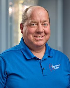 Smiling man in a blue polo shirt standing indoors against a blurred office background