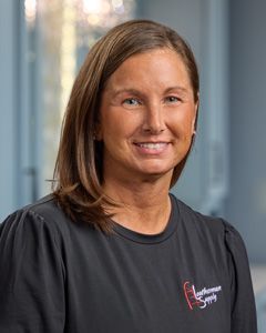 Portrait of a smiling person in a dark T-shirt against a softly lit indoor background