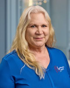 Portrait of a woman in a blue shirt smiling against a softly lit indoor background