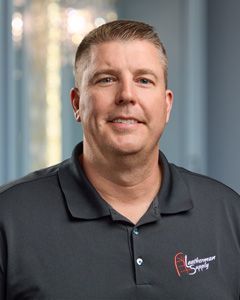 Man in a black polo shirt smiling in a softly lit office setting.