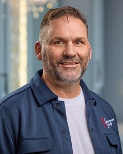 Smiling man in blue work shirt and white T-shirt in an office setting