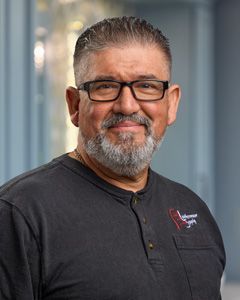 Smiling man with glasses and goatee wearing a black shirt against a blurred indoor background