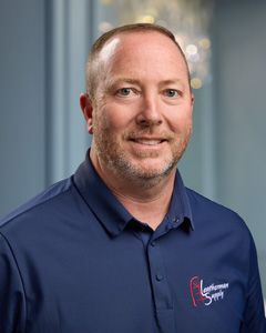 Portrait of a smiling man in a navy polo shirt against a blurred office background