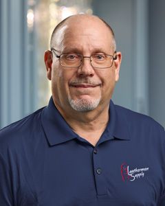 Portrait of a man in a navy polo shirt, smiling against a blurred office background