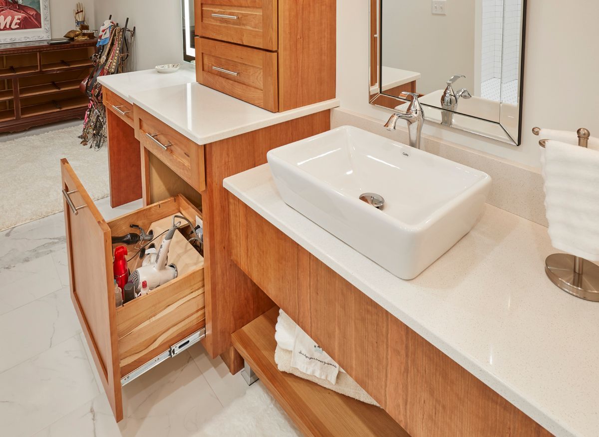 Bathroom vanity with white sink, wood cabinets, and an open drawer showing plumbing supplies