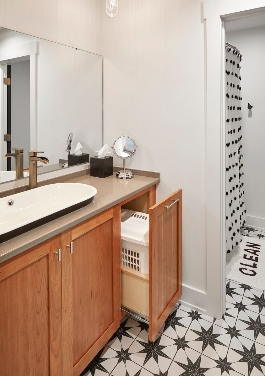 Bathroom vanity with wooden cabinet, large mirror, and black-and-white patterned floor tiles.