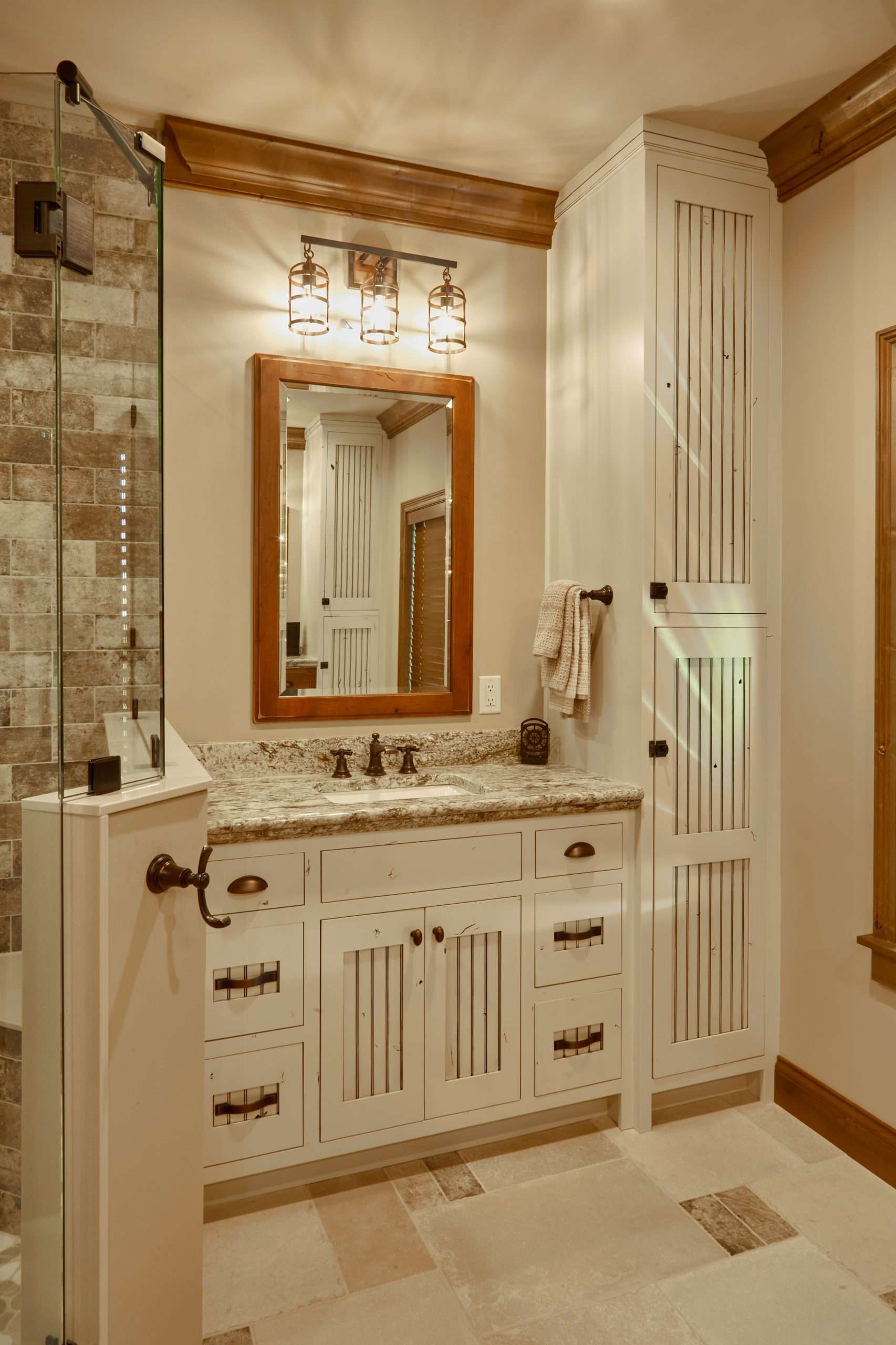 Elegant bathroom with stone tiles, wood vanity, mirror, and tall white cabinet in neutral tones