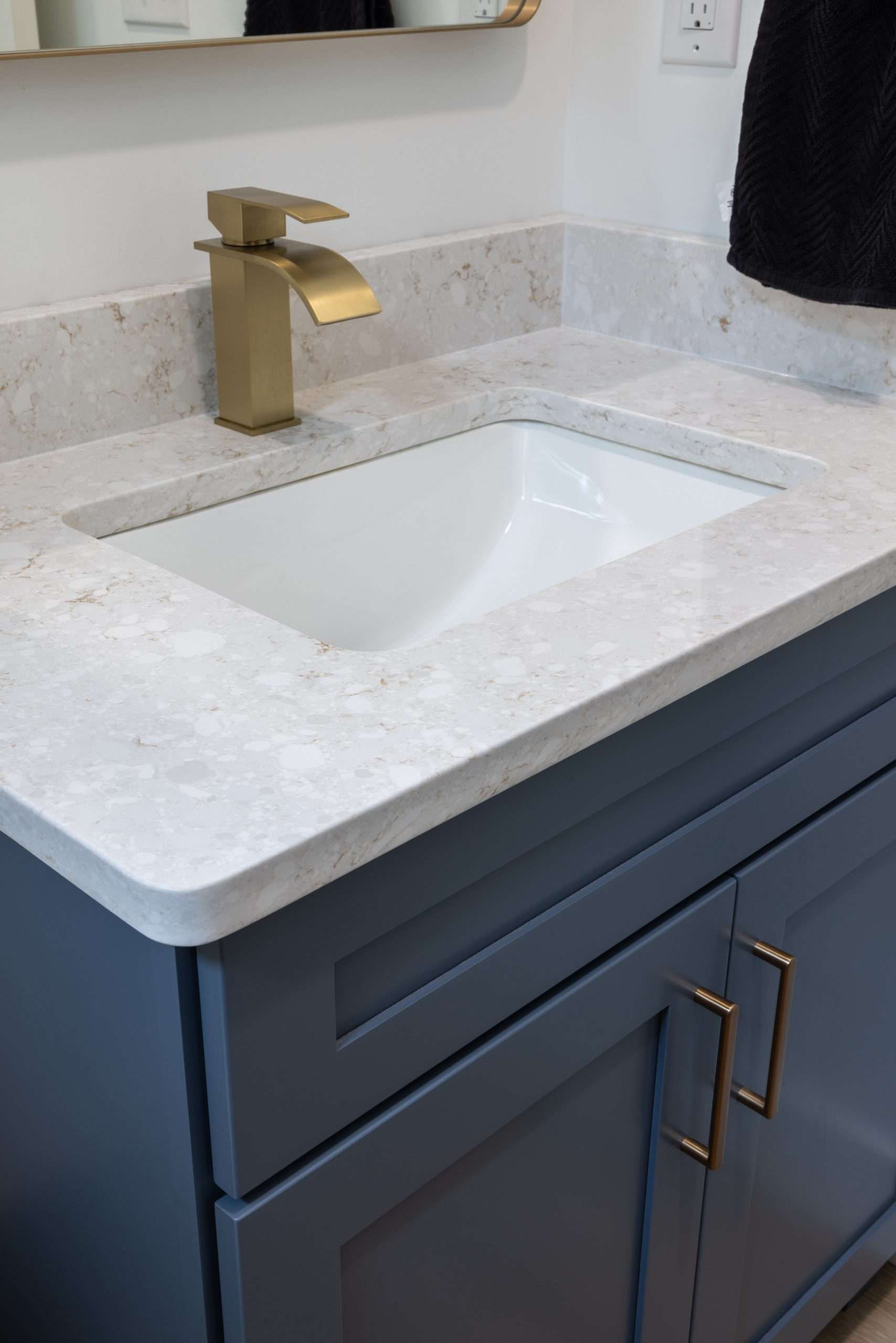 Modern bathroom vanity with white sink, gold faucet, and navy cabinet beside a mirror