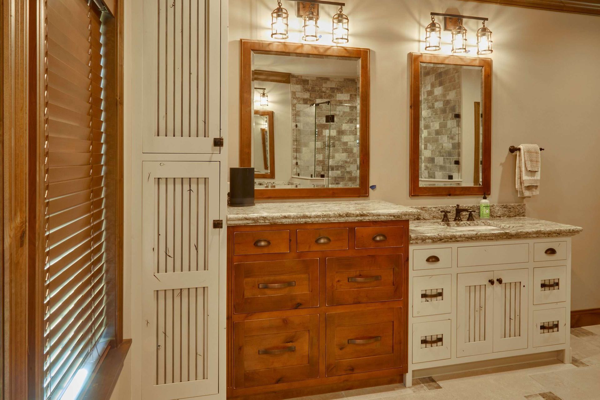 Bathroom vanity with wood cabinets, marble countertop, two mirrors, and wall sconces