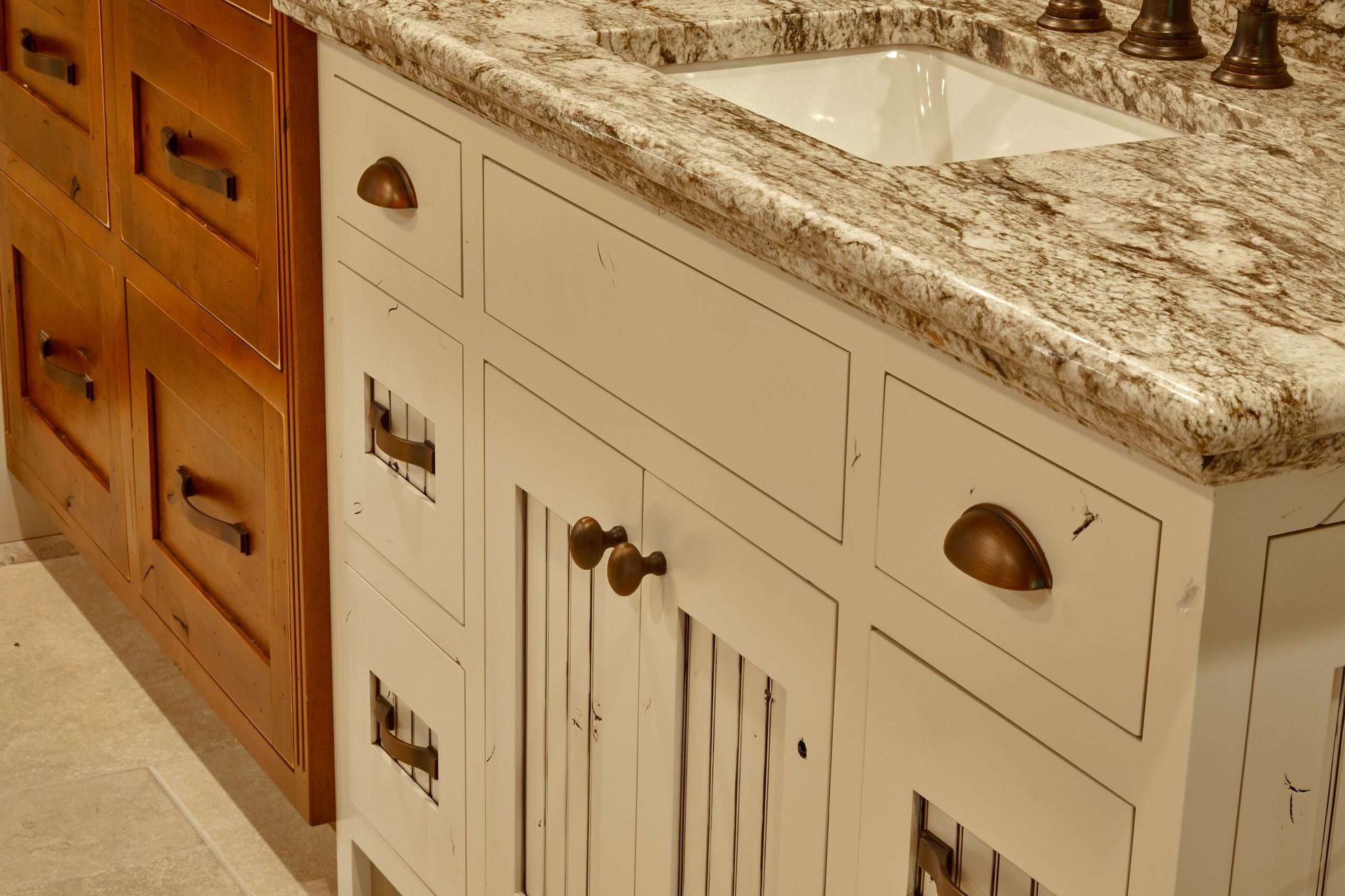 Bathroom vanity with white cabinet, granite countertop, sink, and bronze fixtures next to wood storage drawers