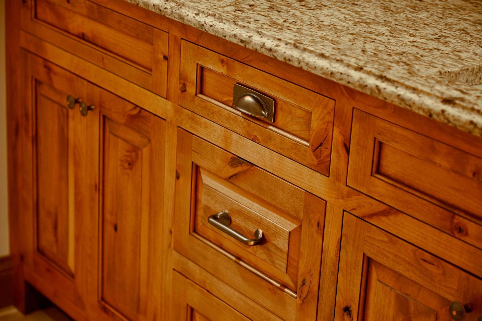 Wooden kitchen cabinets with brass handles beneath a speckled countertop