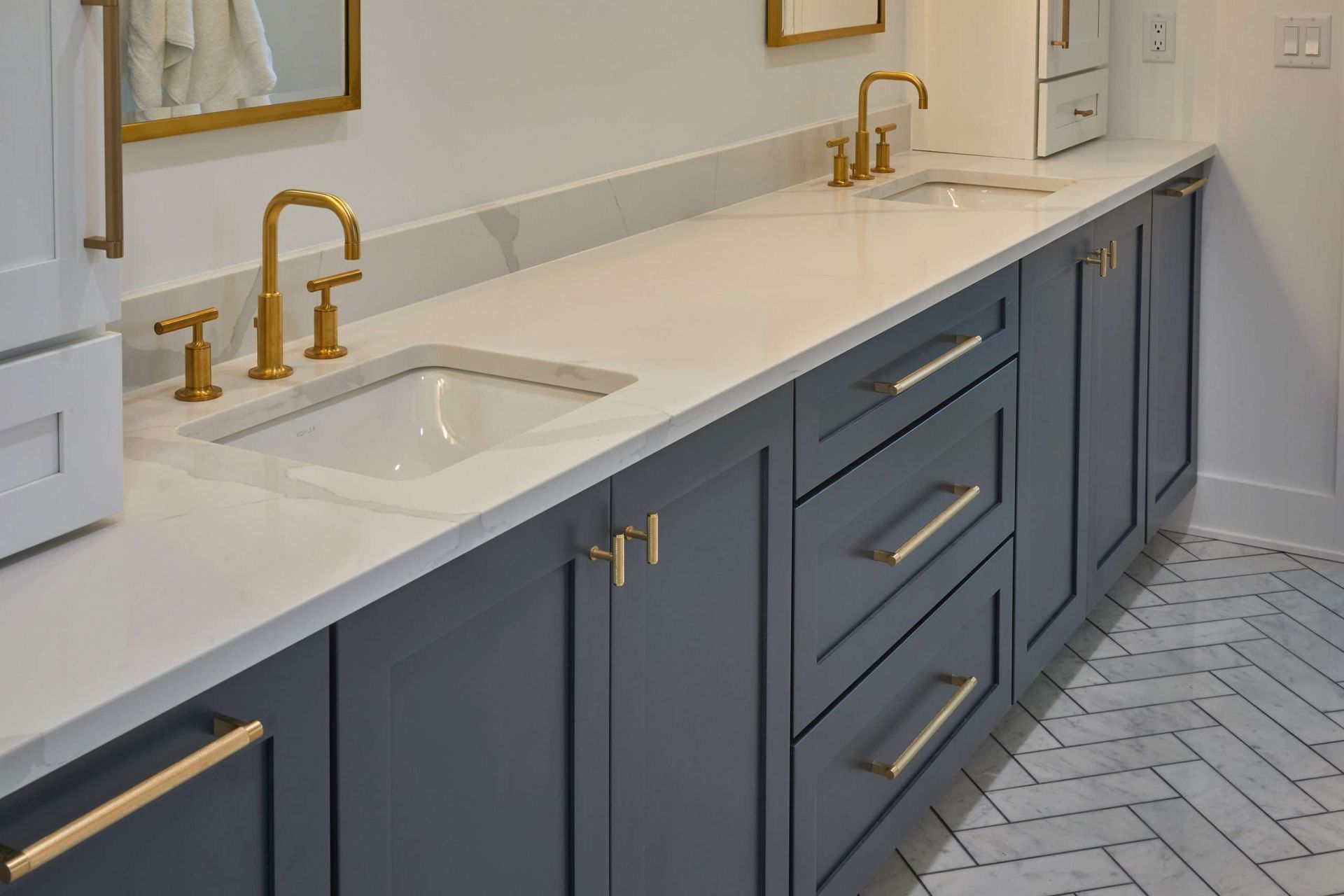 Modern kitchen with navy cabinets, white countertop, brass faucets, and a herringbone tile floor