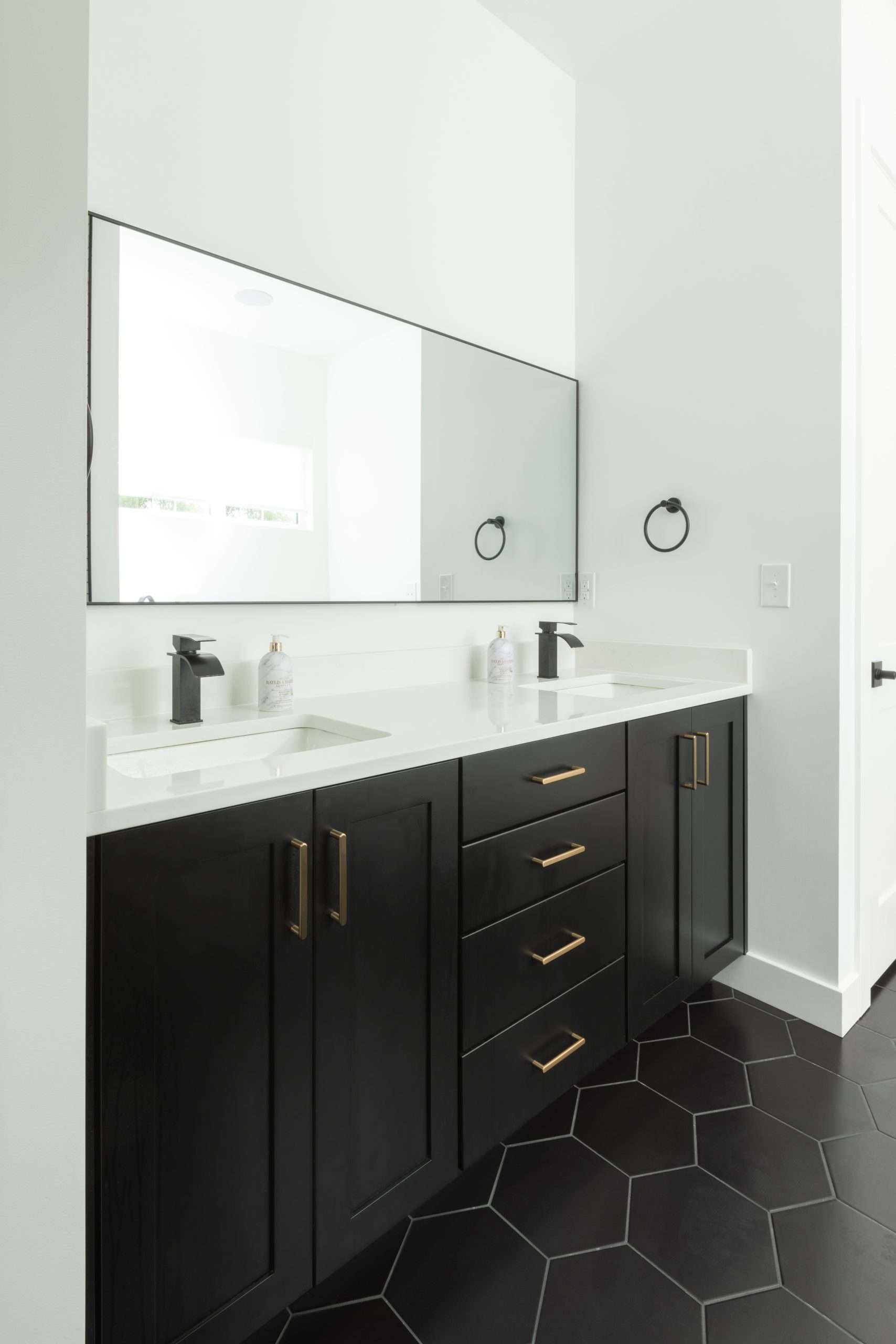 Modern bathroom vanity with black cabinets, white countertop, and large mirror