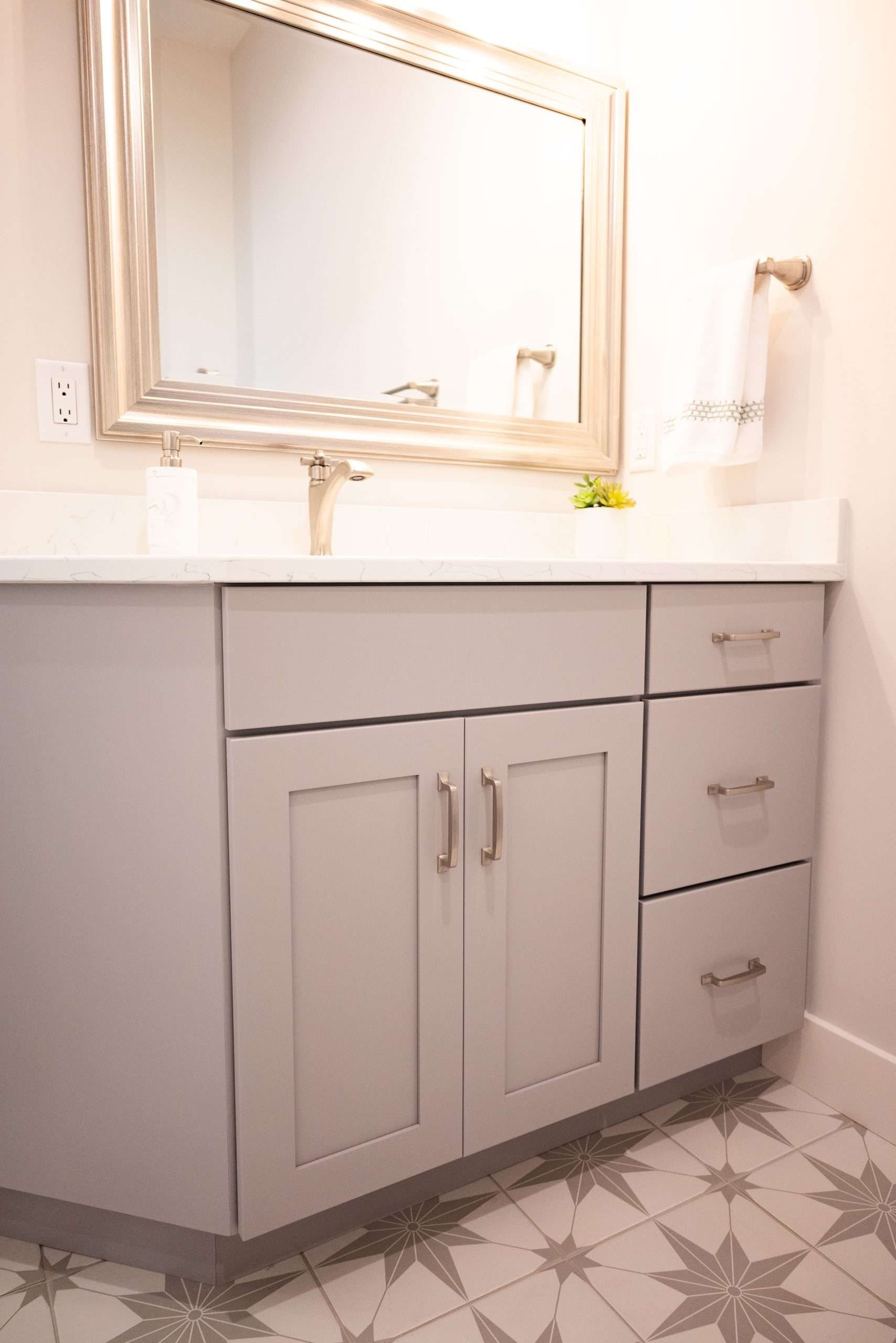 Bathroom vanity with mirror, white countertop, light gray cabinets, and star-patterned tile floor.