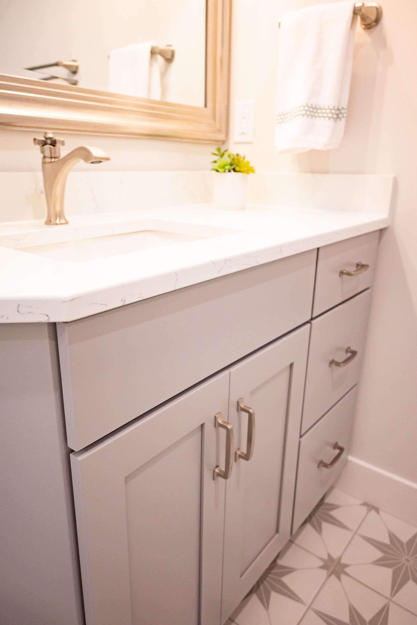 Bathroom vanity with white sink, gray cabinet, gold faucet, and patterned tile floor