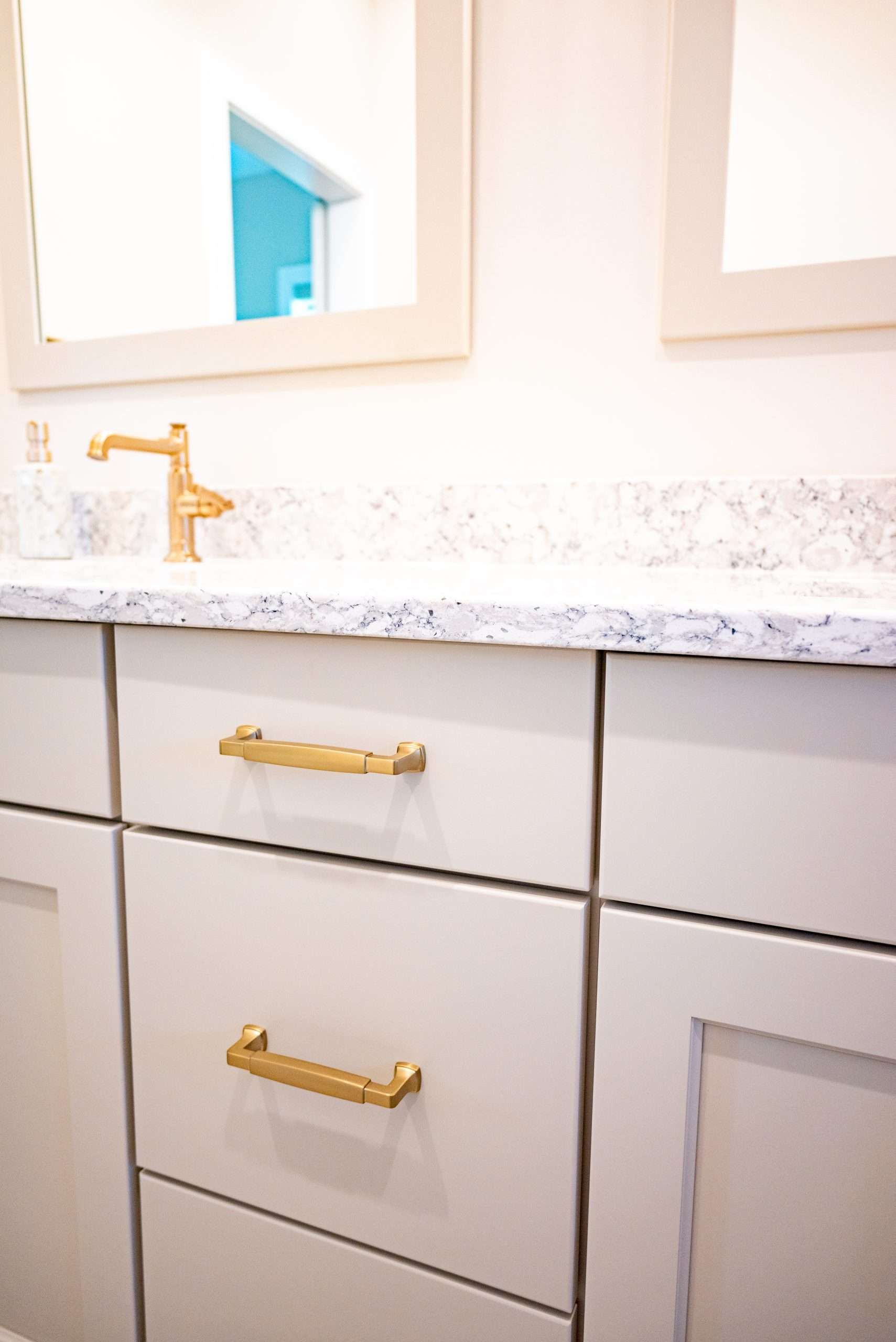 White bathroom vanity with gold hardware, speckled countertop, and mirror above.