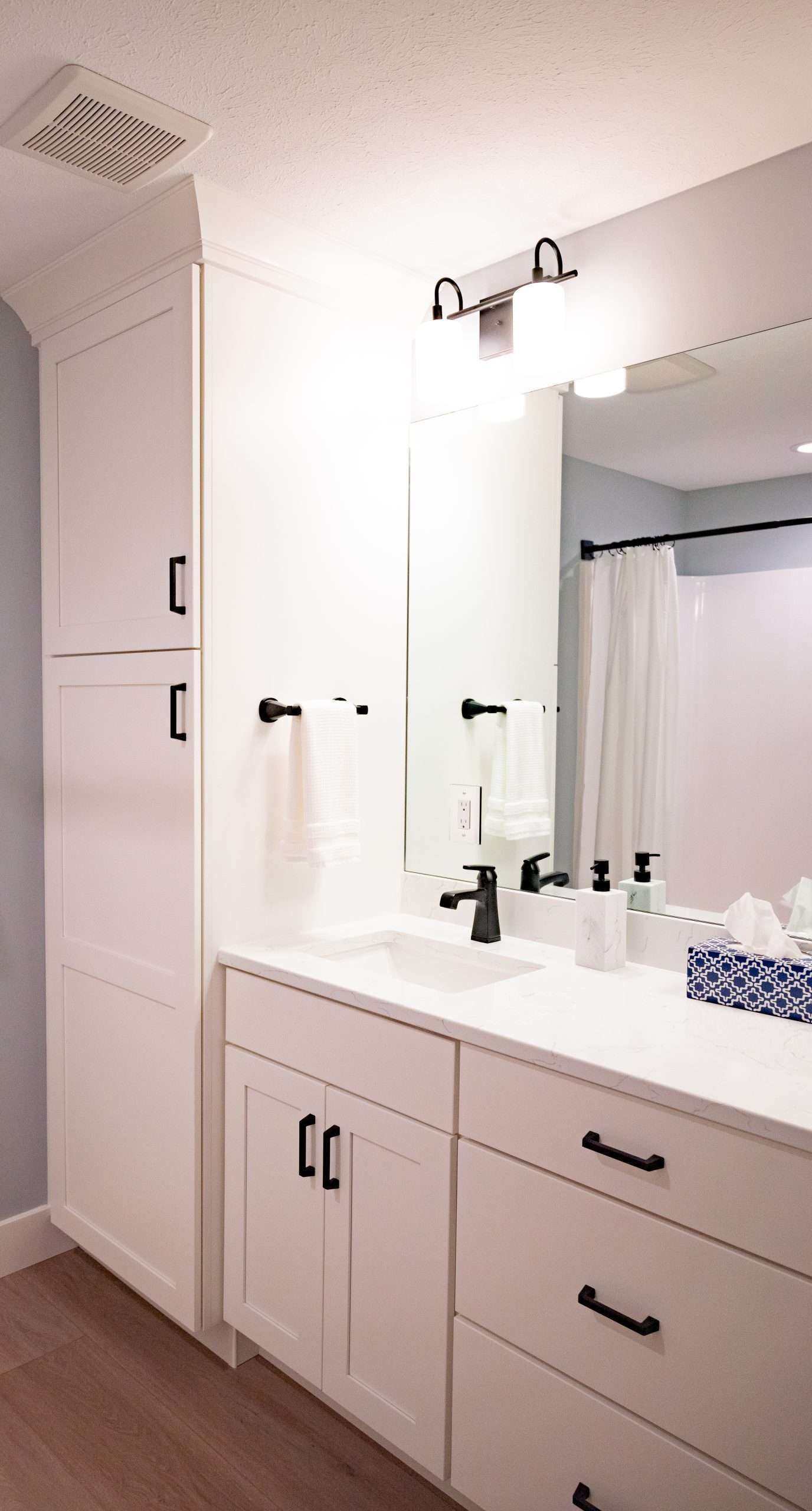 White bathroom vanity with large mirror, black hardware, and built-in cabinet storage.