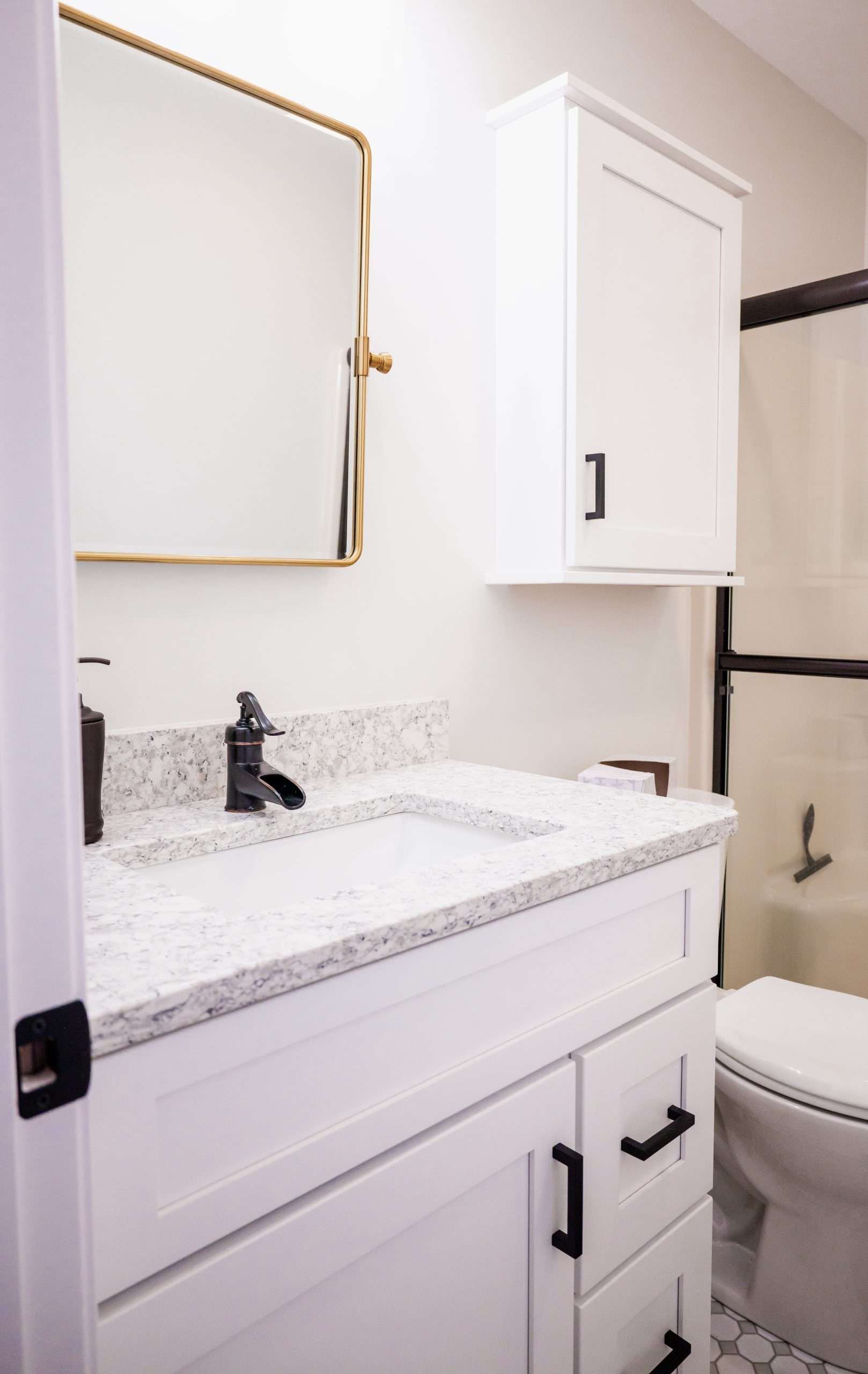 Small white bathroom vanity with sink, mirror, wall cabinet, and toilet beside a shower curtain.