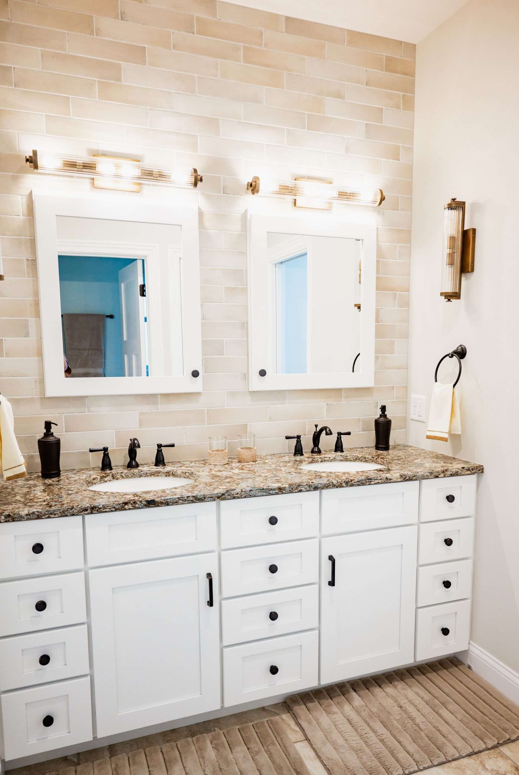 White double-sink bathroom vanity with mirrors, granite countertop, black fixtures, and woven rug
