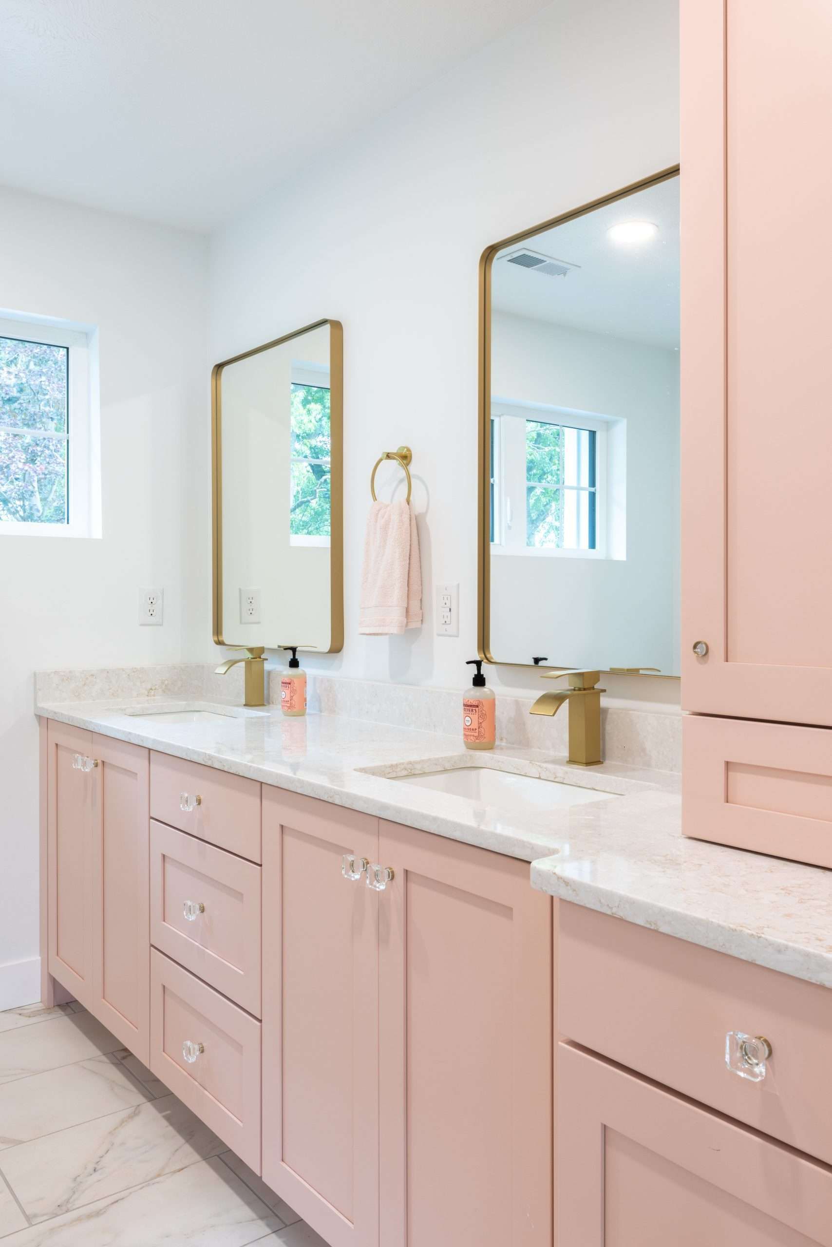 Pastel pink bathroom vanity with double mirrors, white countertop, and gold fixtures in a bright room