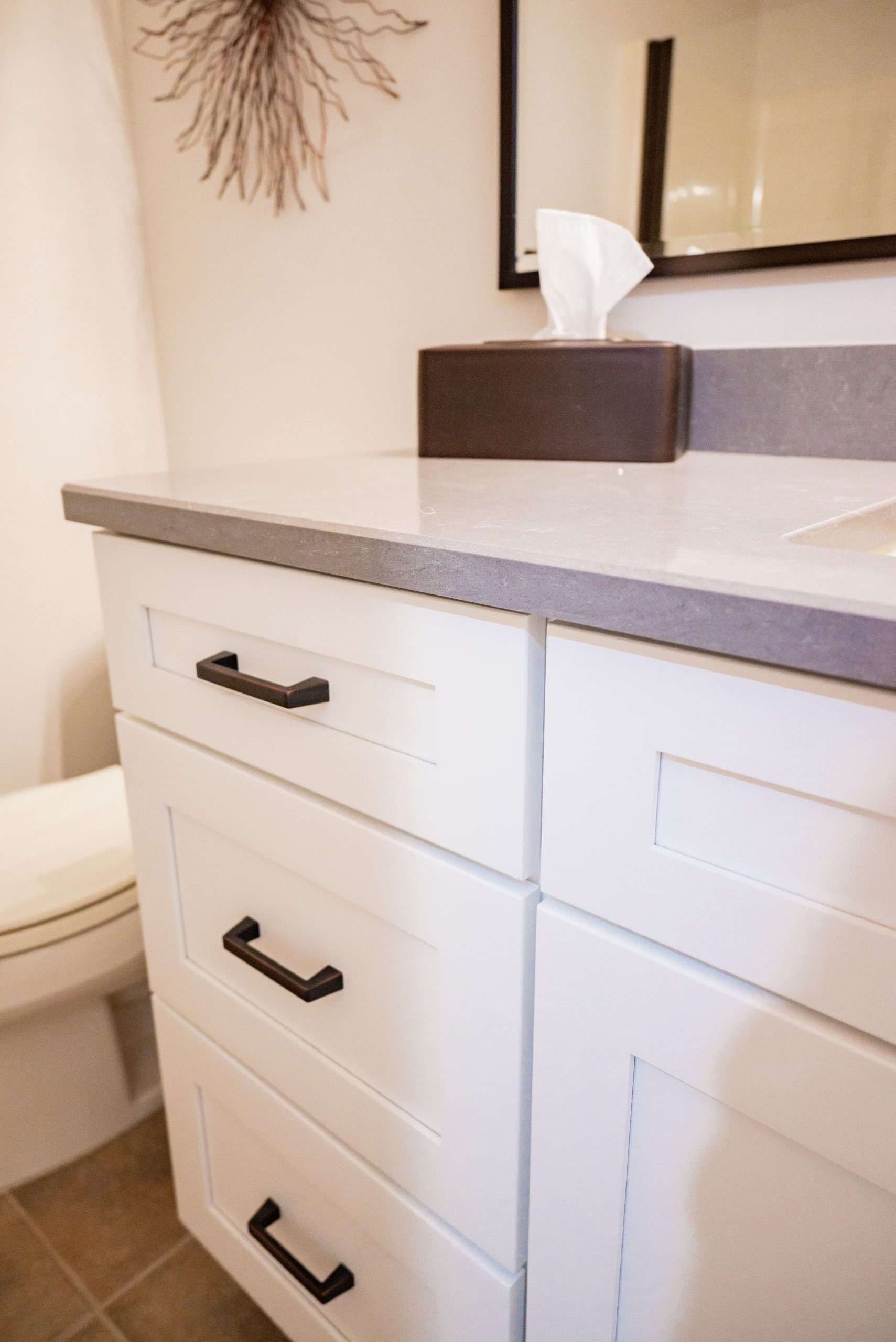 Bathroom vanity with white cabinets, gray countertop, and tissue box near a mirror.