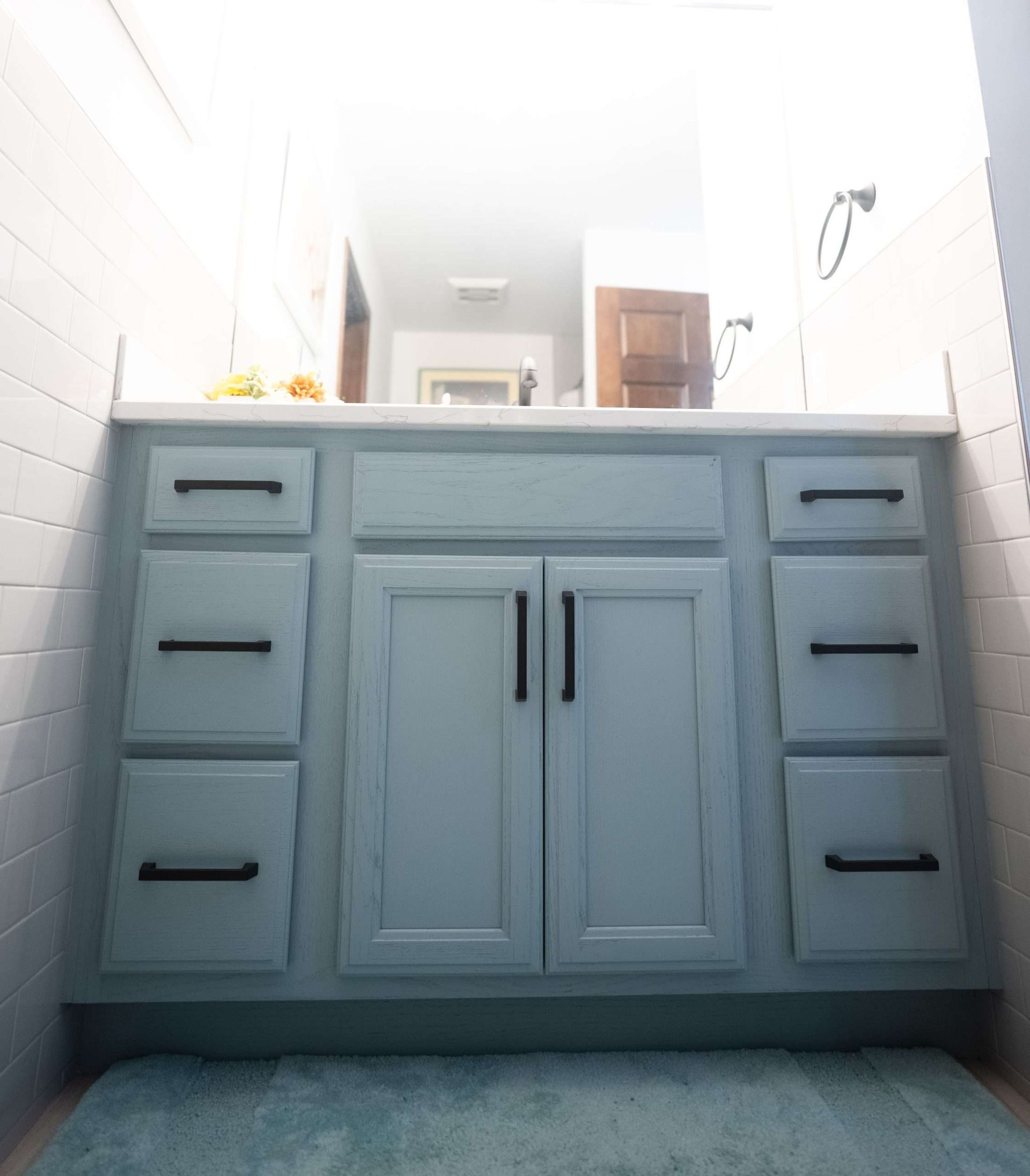 Blue bathroom vanity with drawers, cabinet doors, and sink under a bright mirror
